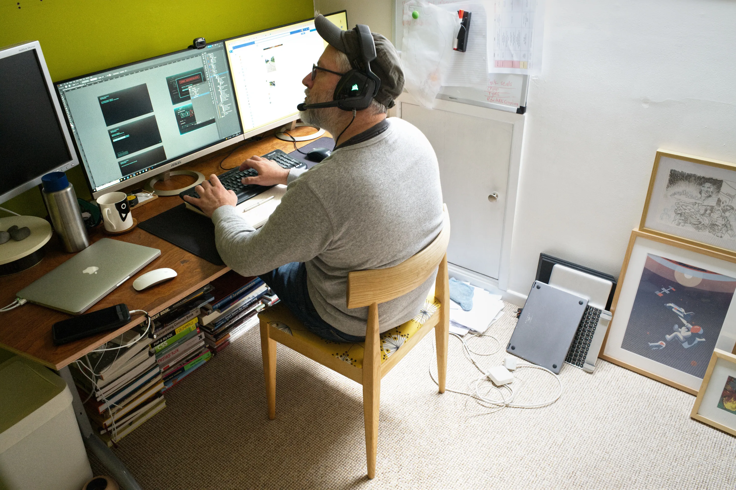 Man with headset at dual monitors, framed prints propped against the wall