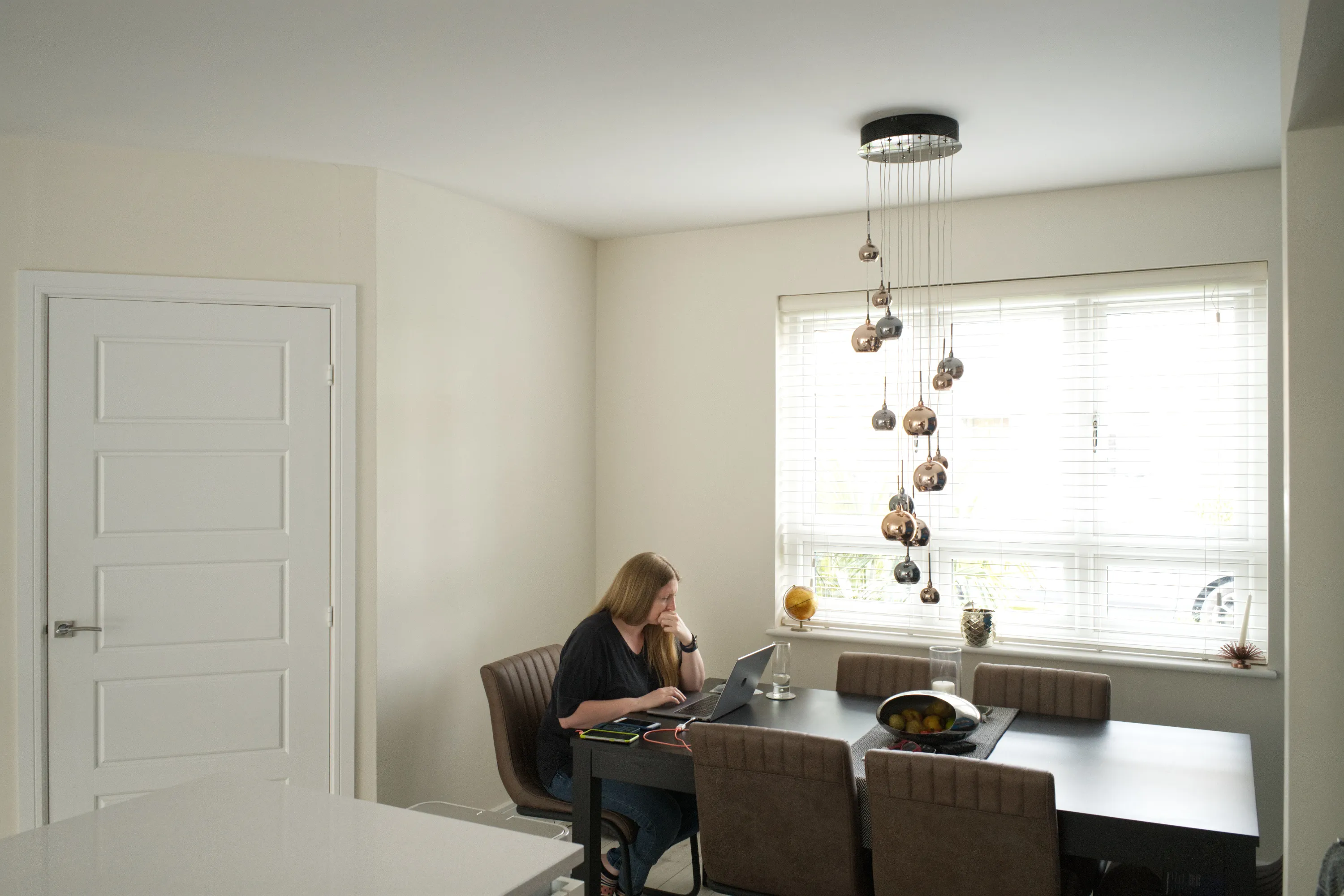 Woman at a dining table with a laptop beneath a cluster pendant light